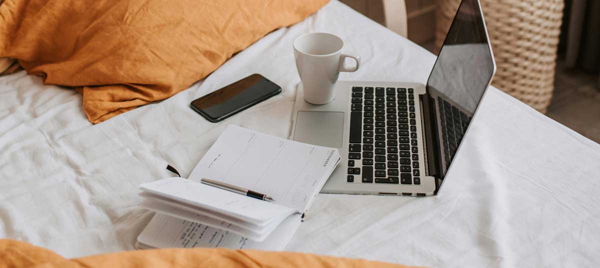 Laptop, coffee, and paperwork arranged on a bed workspace